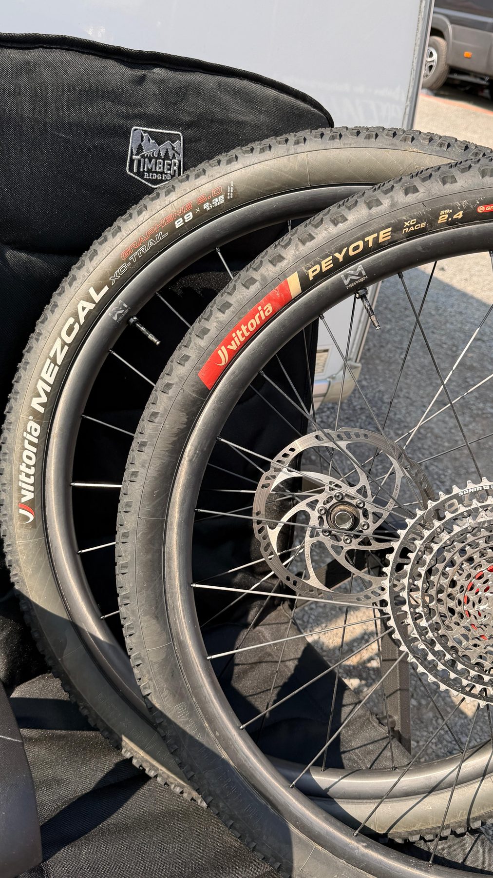 Zwei Laufräder mit Cross-Country-Reifen lehnen im Fahrerlager am Teamfahrzeug.