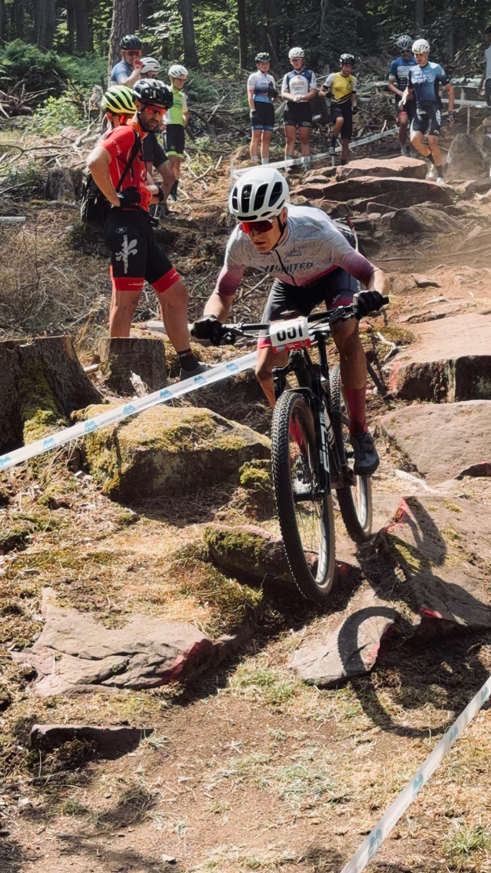Fahrer mit der Startnummer 651 lenkt sein Mountainbike über eine felsige Abfahrt, Zuschauer stehen am Streckenrand.